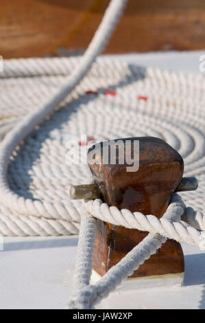 Detail von einem Segelboot-Deck mit zwei Seilen gefesselt auf einem Bitt und einem gerollten Seil im Hintergrund Stockfoto