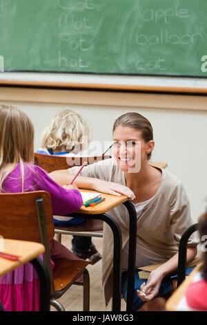 Lächelnde Lehrer kniet neben Schüler Schreibtisch Stockfoto