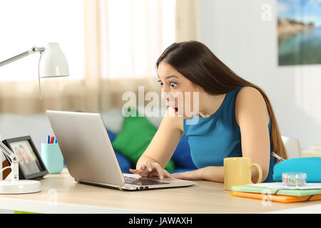 Einzelne begeistert Schüler suchen auf Linie Inhalt in einem Laptop sitzt in einem Schreibtisch in ihrem Zimmer in einem Haus-Interieur Stockfoto