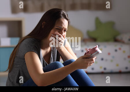 Traurige Mutter vermisst ihre Tochter hält einen kleinen Schuh sitzen auf dem Boden des Schlafzimmers in einem Haus Interieur mit einem dunklen Hintergrund Stockfoto