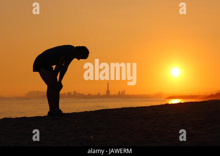 Silhouette der ein müde Sportler bei Sonnenuntergang mit einer Stadt im Hintergrund Stockfoto