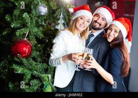 Porträt von fröhlichen Kollegen in Santa caps Toasten mit Champagner Weihnachtsbaum Stockfoto
