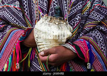 Ein Amaru Mann trägt einen bunten handgewebten Poncho hält eine Schale Horn. Stockfoto