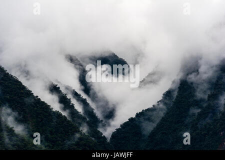 Gewitterwolken verschlingen die steilen bewaldeten Hängen und schroffen Gipfeln der Anden. Stockfoto