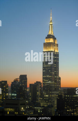 Empire State Building bei Sonnenuntergang mit gelben Turm Lichter zu Ehren von jungen Künstlern und Schriftstellern. Dunklen Silhouetten des nahe gelegenen Gebäuden darunter. -Juni Stockfoto