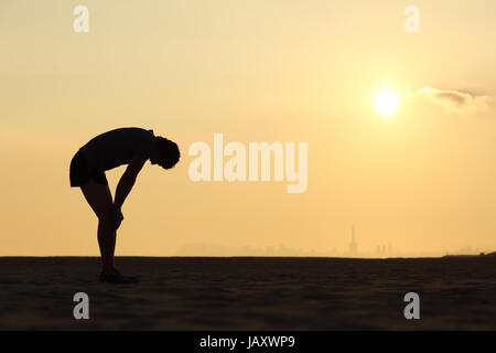 Silhouette von einem erschöpften Sportler bei Sonnenuntergang mit dem Horizont im Hintergrund Stockfoto