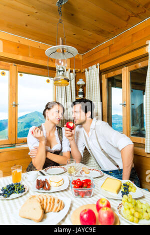 Paar in einem traditionellen Berg Hütte mit einer Mahlzeit, Frühstück mit Obst, Aufschnitt, Käse und Brot Stockfoto