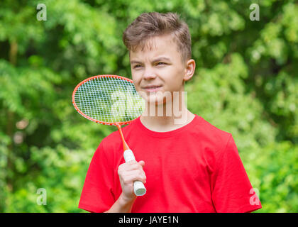 Teen junge Badminton in Wiese mit Wald im Hintergrund spielen. Kind mit Badminton Schläger in der hand. Kinder haben Spaß im Sommerpark am Tag. Stockfoto
