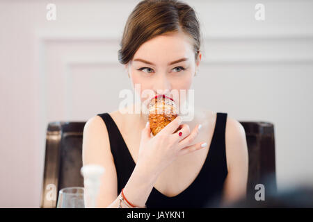 Frau beißt in ein Croissant in einem Cafe innen Stockfoto