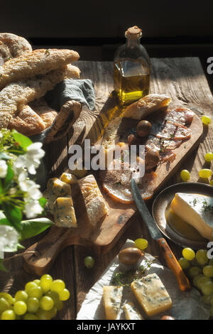 Selbstgebackenes Brot, Käse, Oliven, Jamon und Blumen auf alten Bretter vertikal Stockfoto