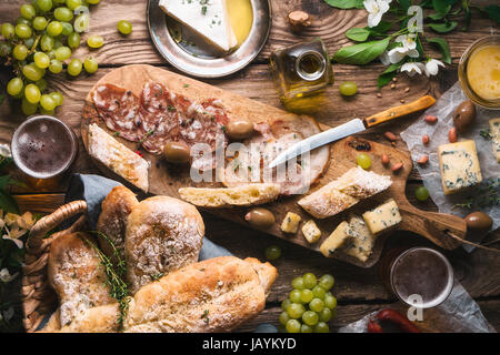 Selbstgebackenes Brot, Käse, Oliven, Trauben und Blumen auf alten Platten horizontal Stockfoto