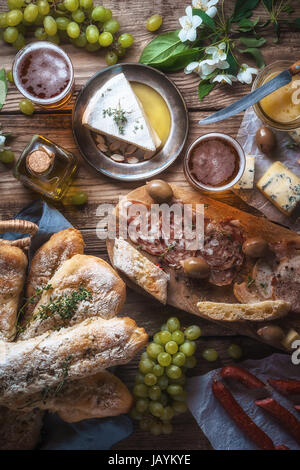 Hausgemachtes Baguette, Käse, Oliven, Trauben und Blumen auf alten Bretter vertikal Stockfoto