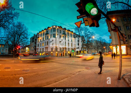 Ein einsamer Fußgänger wartet die Lichter auf grün an einer belebten Kreuzung in Tallinn, Estland. Es ist eine kalte Wartezeit an einem Winterabend. Stockfoto