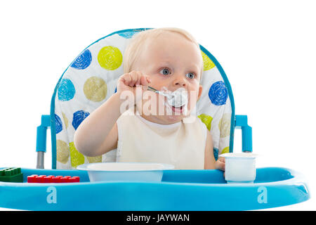 Süßes Baby mit Löffel essen lernen setzt auf Babystuhl auf einem weißen Hintergrund. Stockfoto