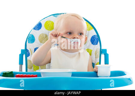 Süßes Baby mit Löffel essen lernen setzt auf Babystuhl auf einem weißen Hintergrund. Stockfoto