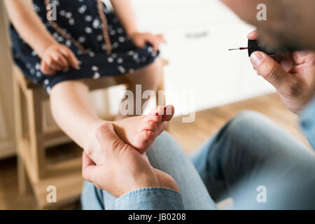 Vater zu Hause Malerei Nägel seiner kleinen Tochter. Stockfoto