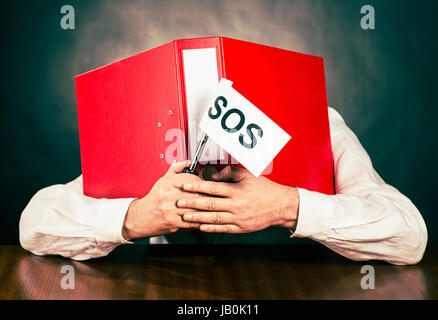 Ein Mitarbeiter verbirgt sein Gesicht hinter einem roten Dateiordner ein SOS-Fahne in der Hand hält. Stockfoto