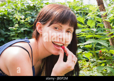 eine junge Frau isst Beeren Himbeeren in einem Garten durch einen canicular Sonnentag Stockfoto