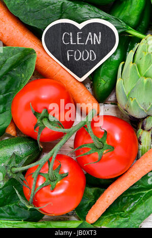 Nahaufnahme von einem herzförmigen Tafel mit dem Text sauber Essen platziert auf einem Stapel von einigen verschiedenen rohes Gemüse wie z.B. Tomaten, Spinat, Karotten oder Stockfoto