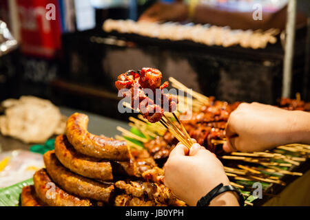 CHIANG MAI, THAILAND - 27 AUGUST: Mann kauft gegrilltes Schweinefleisch am Spieß auf dem Sonntagsmarkt (Walking Street) am 27. August 2016 in Chiang Mai, Thailand. Stockfoto