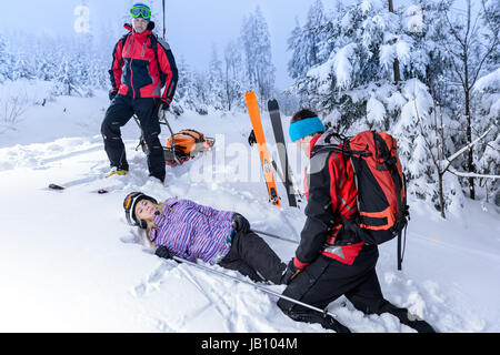 Ski Patrol Hilfe verletzte Frau Skifahrer im Schnee liegend zu retten Stockfoto