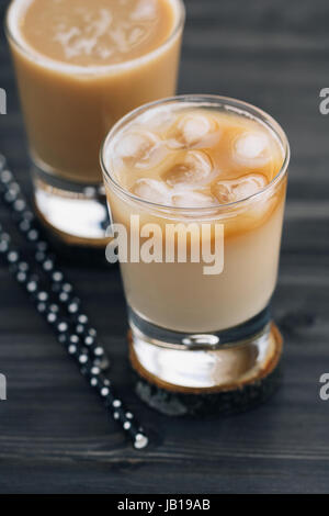 Nahaufnahme von einem erfrischenden Eiskaffee mit Milch in Gläsern auf einem schwarzen Holztisch. Stockfoto