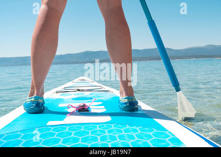 Rückansicht einer Frau stehen auf Stand up Paddel, streichelte das Paddel ins Wasser. Stockfoto