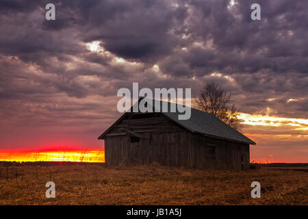 Die April-Sonne geht hinter einem alten Scheunenhaus im ländlichen Finnland. Die Nächte sind bereits im späten Frühjahr ganz weiß. Stockfoto