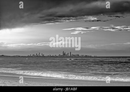 Die Skyline von der Gold Coast City gesehen vom Strand in Coolangatta, Queensland, Australien. Die Abendsonne wirft lange Schatten auf den Wellen. Stockfoto