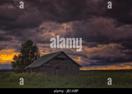 Das Sommer-Gewitter kommt in den Norden Finnlands. Eine einsame Scheunenhaus steht auf den Feldern unter den schweren Wolken. Stockfoto