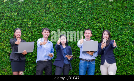 Team von Asian Business-Mann und Frau halten Tablet und feiert Erfolg der Business-Plan vor Büro im grünen Blatt Wand Stockfoto