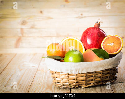 Kleiner Weidenkorb köstliche verschiedene Obstsorten mit einen Apfel und eine Vielzahl von Zitrusfrüchten, darunter ein saftiges halbiert Orange auf hölzernen Hintergrund Stockfoto