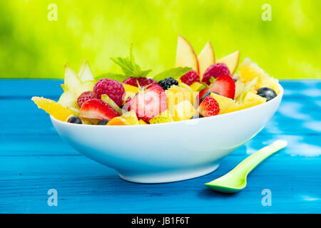 Schüssel mit bunten leckere tropische Früchte Salat mit einer Auswahl von reifen Früchten, einschließlich Strawbwerries, Himbeeren, Äpfel und Zitrusfrüchte, gekrönt mit einem Zweig Minze Stockfoto