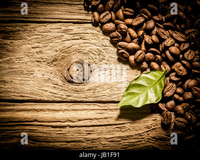 Draufsicht auf einen Haufen von frisch gebratenen Kaffeebohnen auf verwitterten knorrigen Treibholz Bohlen mit frischen grünen Kaffee Blatt, Vignettierung und Exemplar Stockfoto