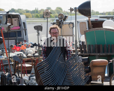 Ein Standbesitzer am Sunbury Antiquitäten Messe Kempton Park London schiebt einen Stapel von Stühlen Stockfoto