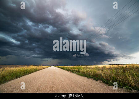 Leere Schotterstraße durch ein Feld mit dramatischen Wolken und stürmischem Himmel in Rockwood, Texas Stockfoto