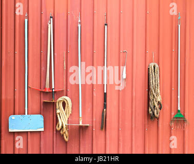 Landwirtschaftliche Geräte hängen rote Scheune Wand Stockfoto