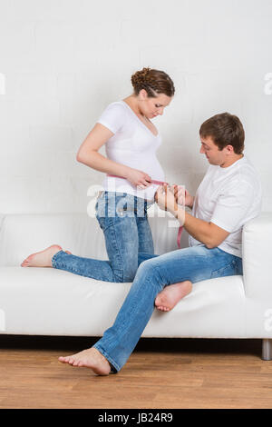 Glücklich schwanger Familie mit Maßband sitzen auf dem Sofa im Zimmer. Stockfoto