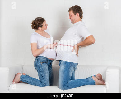 Glücklich schwanger Familie mit Maßband sitzen auf dem Sofa im Zimmer. Stockfoto