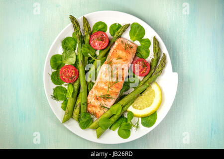 Eine obenliegende Foto einer Platte gegrillter Lachs mit grünem Spargel, Kirschtomaten, Feldsalat und einer Scheibe Zitrone, eine gesunde Ernährung-Schale mit einer pla Stockfoto