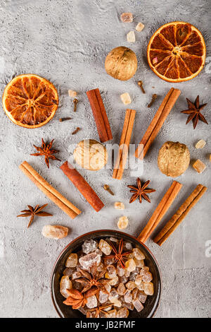 Verschiedene Arten der Gewürze - Zimt, Nelken, Anis Sterne, Walnüsse, getrocknete Orangenscheiben, karamellisierten braunen Zucker auf grauem Beton Hintergrund. Top vi Stockfoto