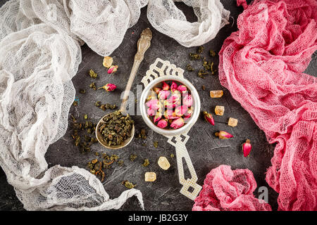 Rosenknospen in einem kleinen Metall Sieb trocknen, und grüner Tee in den Löffel und karamellisierten braunen Zucker trocken. Stockfoto