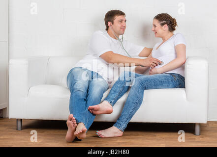 Die glückliche schwangere Frau mit dem Mann sitzt auf einem Sofa des Hauses. Stockfoto