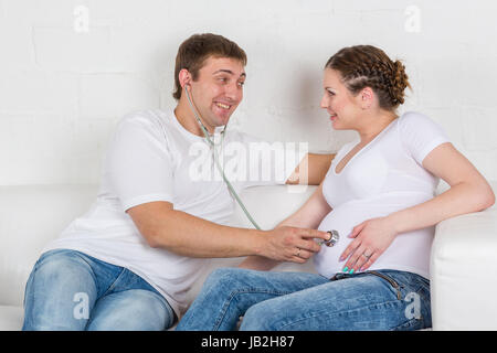 Die glückliche schwangere Frau mit dem Mann sitzt auf einem Sofa des Hauses. Stockfoto