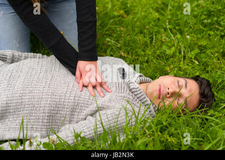 Schöne Frau, erste Hilfe, ein hübscher junger Mann, Herz-Lungen-Wiederbelebung, in einem Rasen Hintergrund geben. Stockfoto