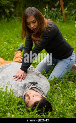 Schöne Frau, erste Hilfe, ein hübscher junger Mann, Herz-Lungen-Wiederbelebung, in einem Rasen Hintergrund geben. Stockfoto