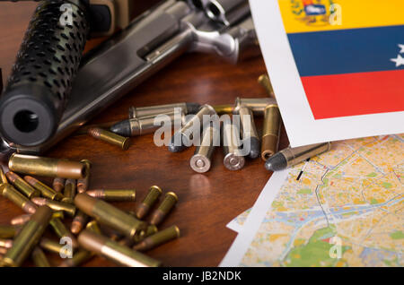 Nahaufnahme von einer Schrotflinte und einem Revolver, Patronengürtel mit Kugeln mit einer unscharfen venezolanische Fahne, Holztisch. Stockfoto