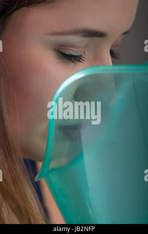 Nahaufnahme einer schönen Frau, die Inhalation mit einem Vaporizer Vernebler Maschine auf grauem Hintergrund zu tun. Stockfoto