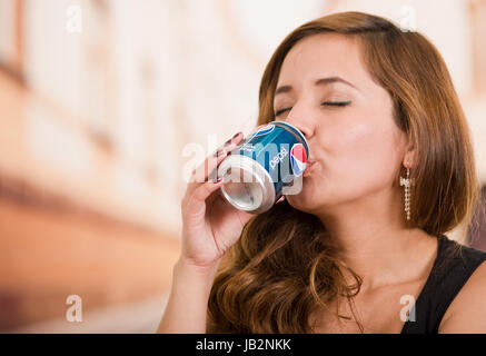 Quito, Ecuador - 6. Mai 2017: Hübsche junge Frau trinkt Pepsi in unscharfen Stadt Hintergrund. Stockfoto