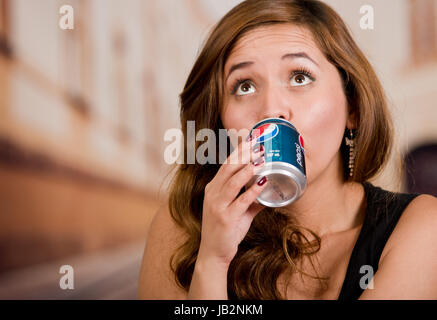 Quito, Ecuador - 6. Mai 2017: Hübsche junge Frau trinkt Pepsi in unscharfen Stadt Hintergrund. Stockfoto